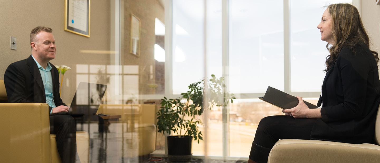 A man and woman seated in chairs in an office, facing each other.