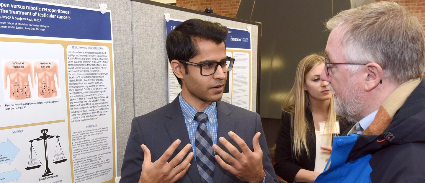 Student wearing a blue suit presenting his project to a professor