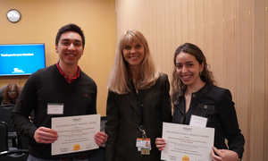 Two students holding certificates with one faculty member