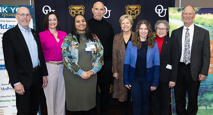 A group of people smiling in front of an OU background