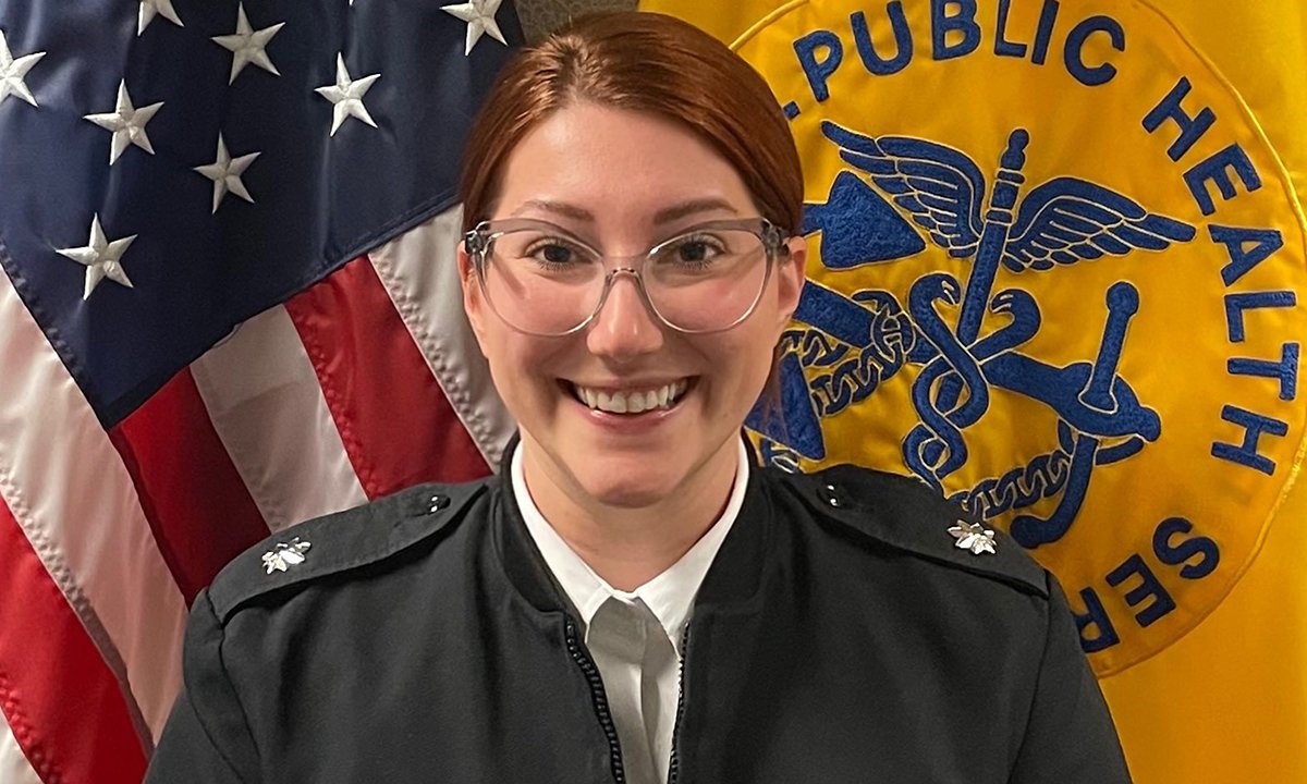 A woman in uniform in front of two flags.