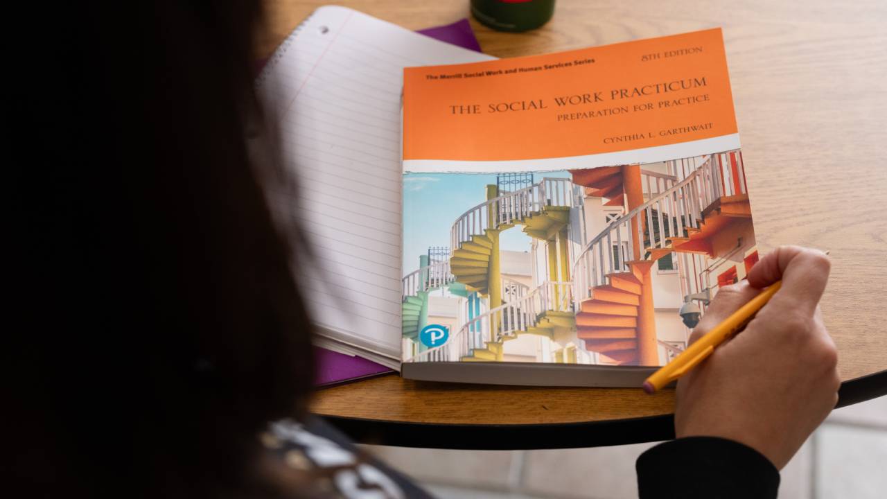 Female student from behind looking at social work textbook