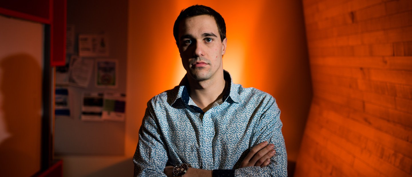 Male MBA student standing with his arms crossed in a dimly lit room