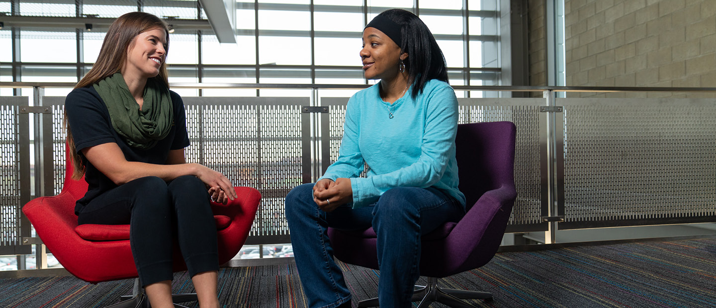 Image of two ladies sitting in chairs facing each other smiling.