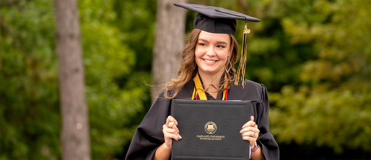 Student in a cap and gown smiling at camera with diploma