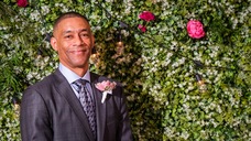 Darryl Hill posing for a photo in front of a wall of flowers