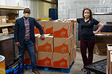 image of two OU employees standing in a warehouse-style room with big boxes and wearing masks