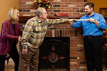 Two physical therapists assist and measure an elderly man as he reaches his arm