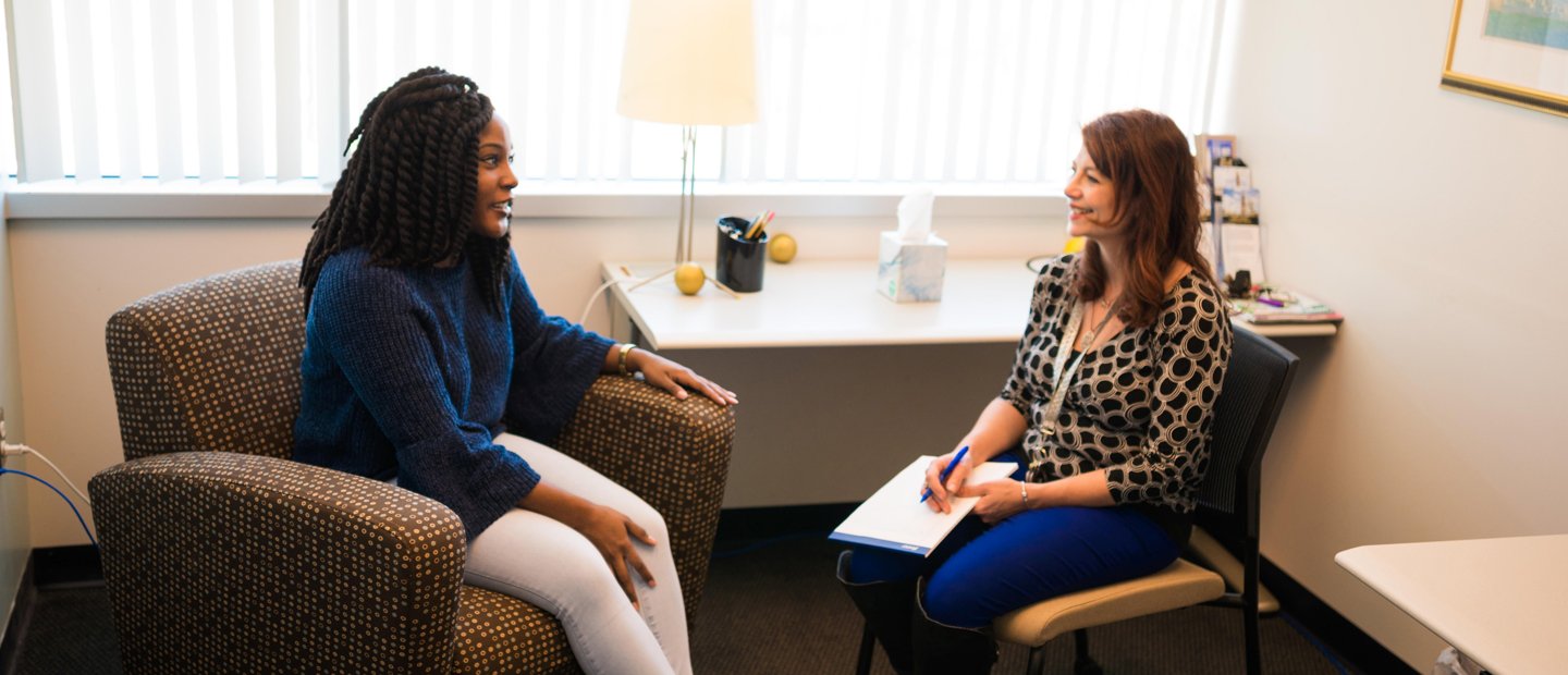 Two women seated in an office, facing each other, smiling.