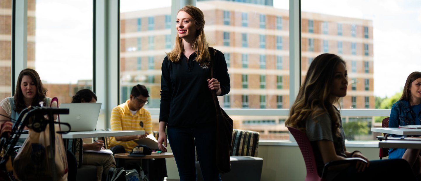 A young woman stands smiling in the Honors College building